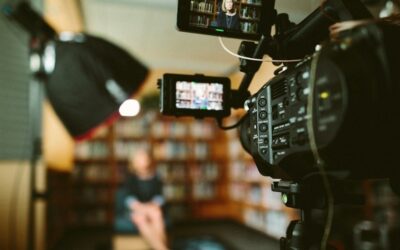 Videokamera kuvaa henkilöä kirjahyllyjen edessä haastattelutilanteessa